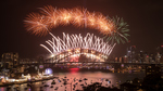 Fireworks at night over a bridge. Boats on the river under the bridge.