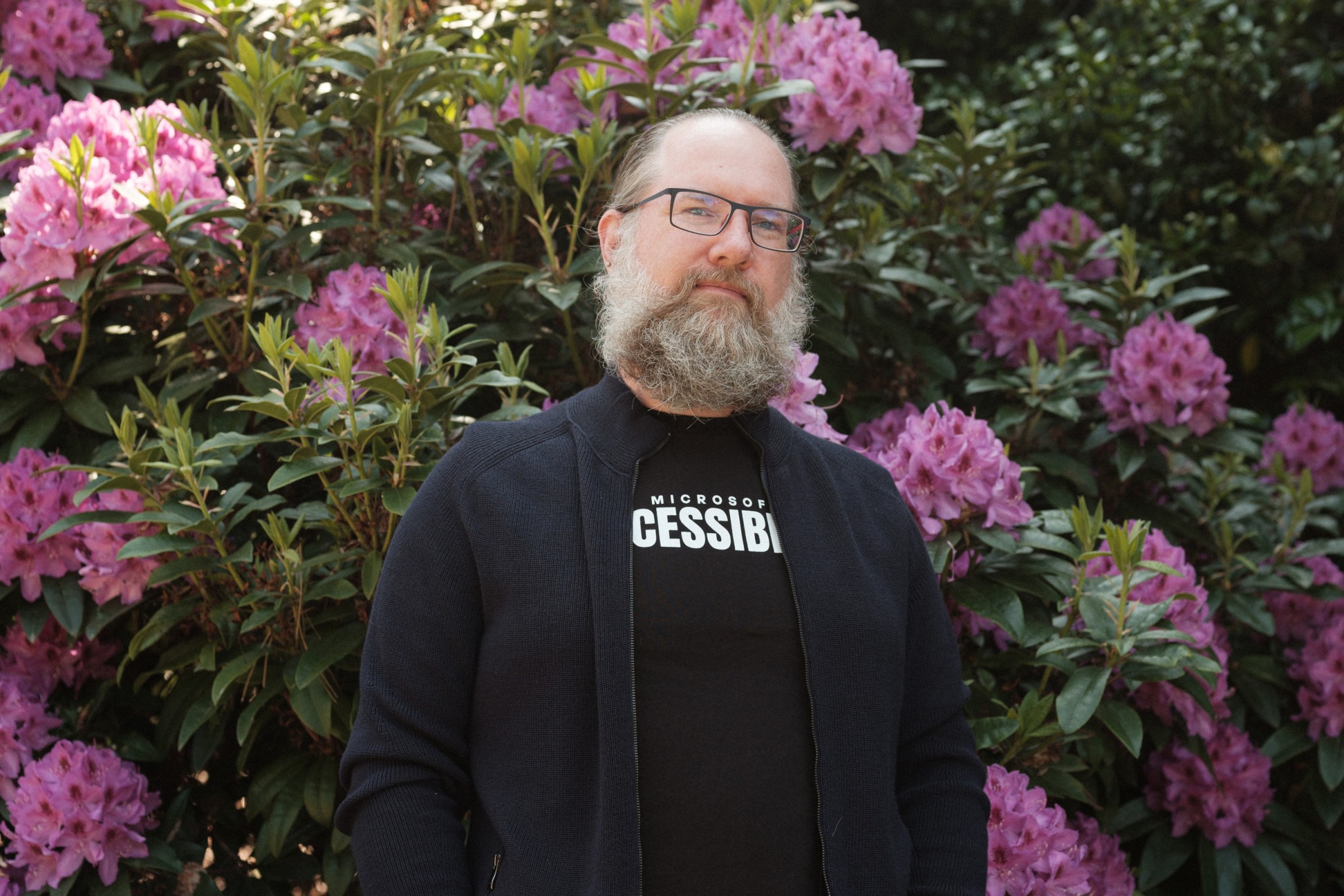 Aaron stands smiling in front of flowering bushes.