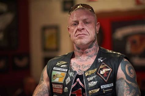 a man with tattoos and piercings on his chest wearing a leather vest, looking at the camera