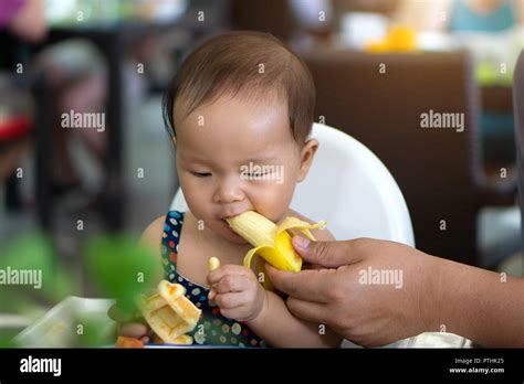 Cute asian toddler baby girl eating banana Stock Photo - Alamy