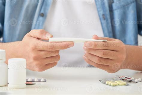 Sick young man looks at a thermometer 12746230 Stock Photo at Vecteezy