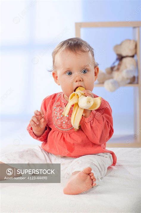 Adorable baby girl eating banana. - SuperStock