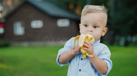 Cheerful 1 Year Old Baby is Eating a Banana. it`s Standing on the Back ...