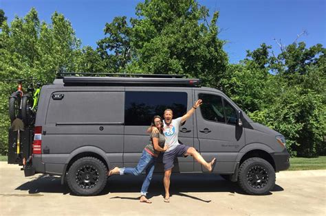 A gun metal grey Sportsmobile 4x4 custom camper van conversion with happy owners standing next ...