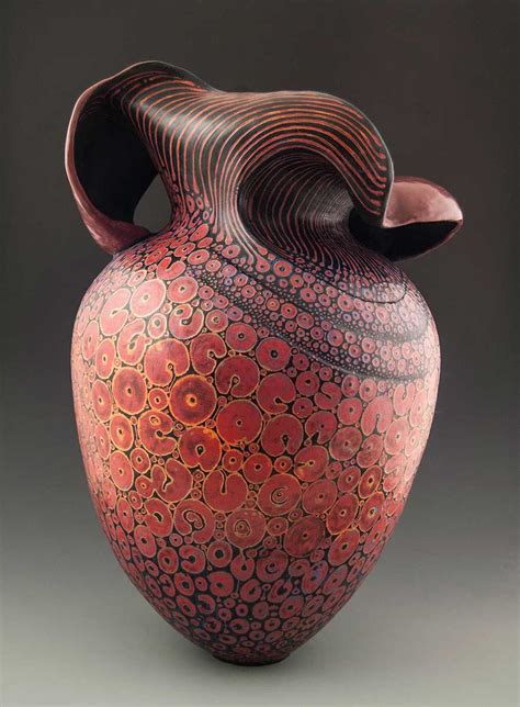 a red and black vase sitting on top of a gray table next to a wall