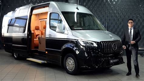 a man in a suit standing next to a black and silver mercedes benz minibus