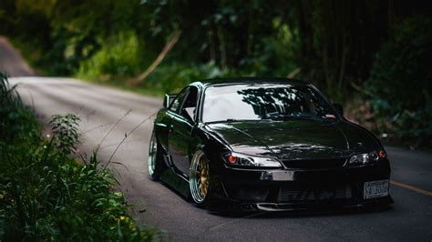 a black car parked on the side of a road next to some bushes and trees