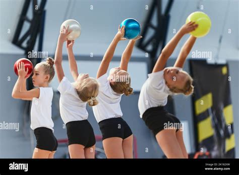 Little girls, beginner gymnastics athletes doing exercises with gymnastics equipment at sports ...