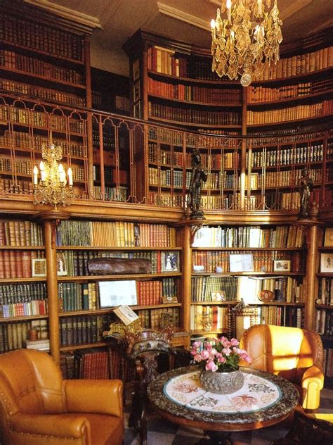 a room filled with lots of books and chairs next to a chandelier hanging from the ceiling