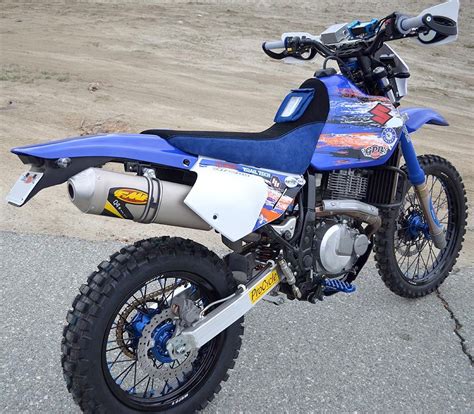 a blue and white dirt bike parked on top of a cement road next to a field