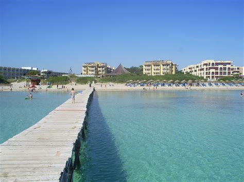 people are on the beach and in the water near a pier that extends into the ocean