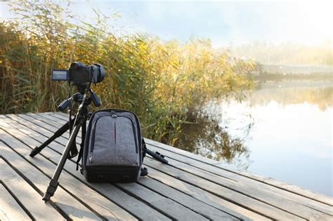 Premium Photo | Tripod with modern camera and backpack on wooden pier near water professional ...