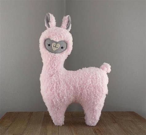 a pink llama stuffed animal sitting on top of a wooden table next to a gray wall