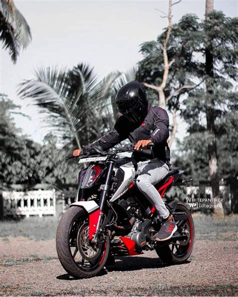 a man riding on the back of a red and white motorcycle in front of palm ...