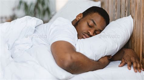 African Man Sleeping Hugging Pillow Lying In Bed At Home Stock Photo by Prostock-studio