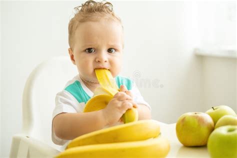 Funny Baby Boy Sitting at the Table in Child Chair Eating Banana on ...