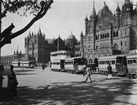 an old black and white photo of people walking in front of a building with two buses parked on ...