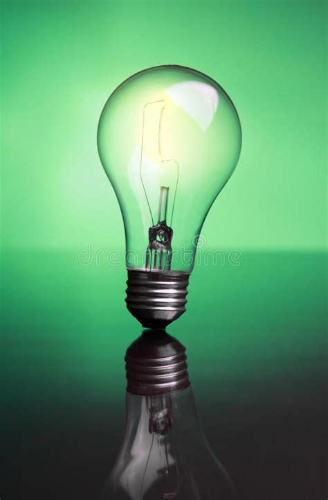 Glowing lightbulb. A glowing lightbulb on a reflective surface with a green back , #SPONSORED, # ...