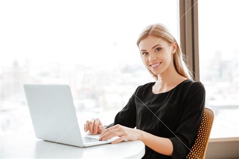 Happy young woman working in office with laptop, typing and looking at camera. Royalty-Free ...