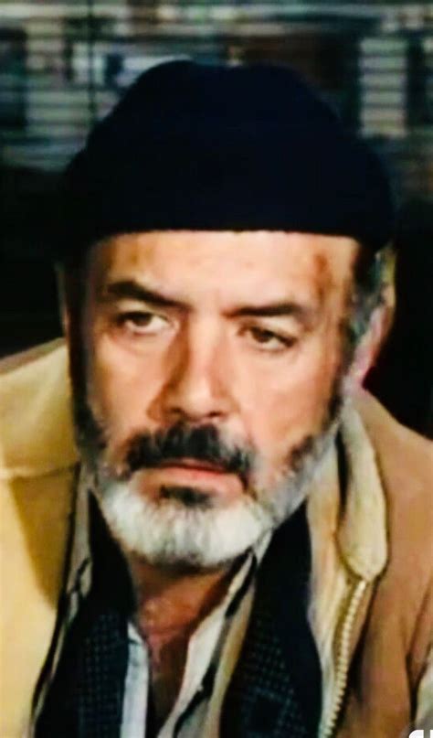 an old man with a beard wearing a black hat and jacket is looking at the camera