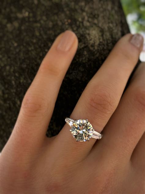 a woman's hand with a diamond ring on top of her finger, next to a rock