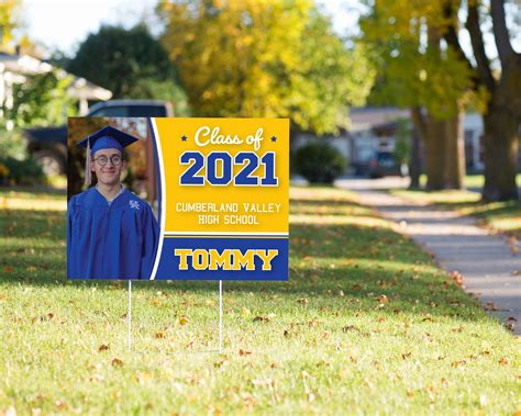 a blue and yellow yard sign with a photo of a graduate on it in the grass