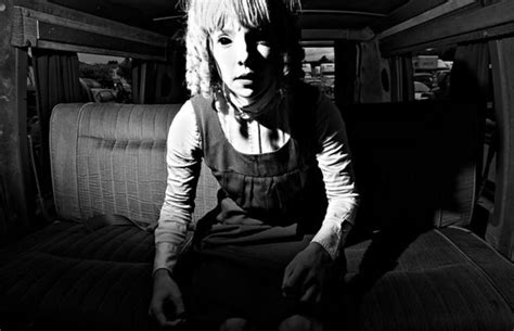 a black and white photo of a woman sitting in the back of a truck with her hands on the seat