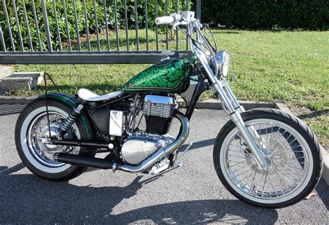 a green and black motorcycle parked on the side of a road next to a fence