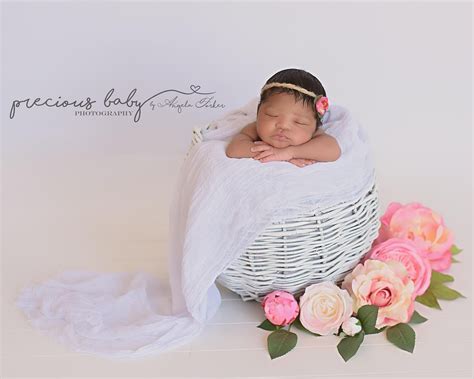 Gorgeous newborn African American baby girl sleeping in a white basket surrounded by beautiful ...