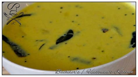 a white bowl filled with yellow soup on top of a wooden table next to a spoon