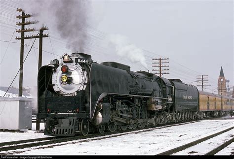 a black train traveling down tracks next to power lines and telephone poles in the snow