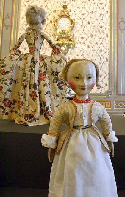 an old fashion doll is displayed in front of a wallpapered room with two mannequins