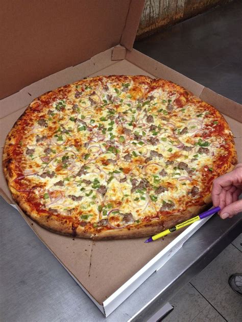 a large pizza sitting inside of a box on top of a counter next to a person's hand