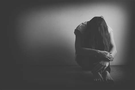 Teenager girl with depression sitting alone on the floor in the dark room. Black and white photo ...