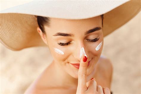 Beautiful Young woman with sun cream on face. Girl holding sunscreen bottle on the beach. Female ...