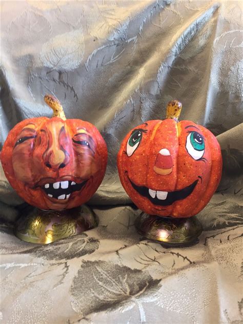 two pumpkins with faces painted on them are sitting on a silver cloth covered surface