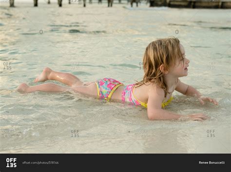 Girl lying on stomach in water at beach stock photo - OFFSET