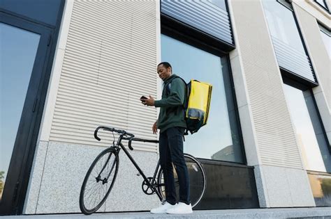 Premium Photo | An africanamerican courier with a yellow backpack walks with a bicycle along an ...