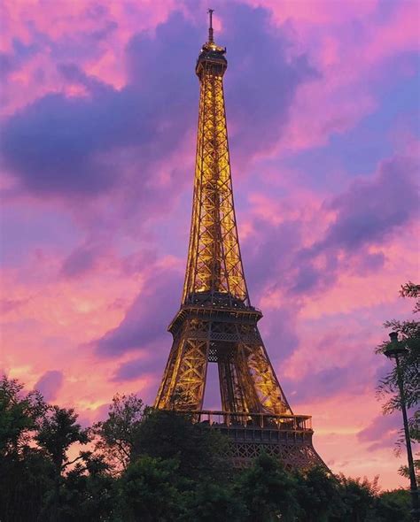 Eiffel Tower at sunset with Pink and purple sky. The tower is lit with yellow lights at twilight ...