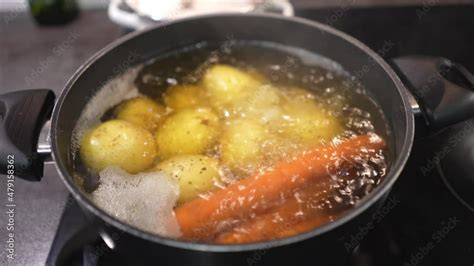 Slow Motion video of potatoes and carrots in the boiling water. cooking raw vegetables in pan ...