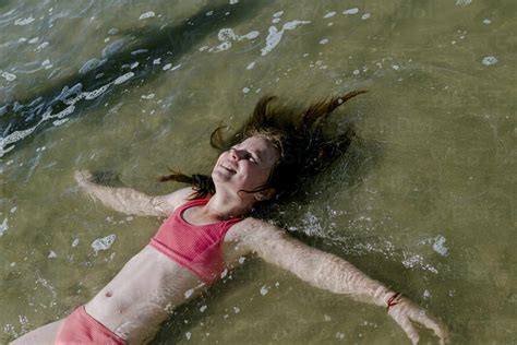 Girl lying down in water at beach on sunny day stock photo