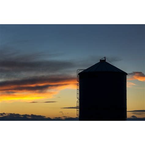 Silhouette of large metal grain bin with colourful clouds at sunset with blue sky; Alberta ...