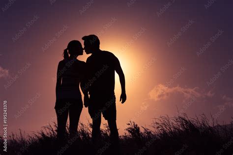 Silhouette of young couple holding holding hands kissing at sunset ...