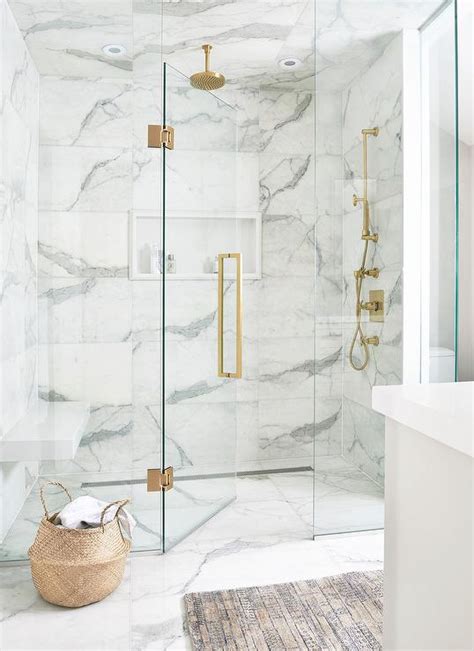 Luxurious white and gray marble shower with a white niche enclosed with glass doors and ...