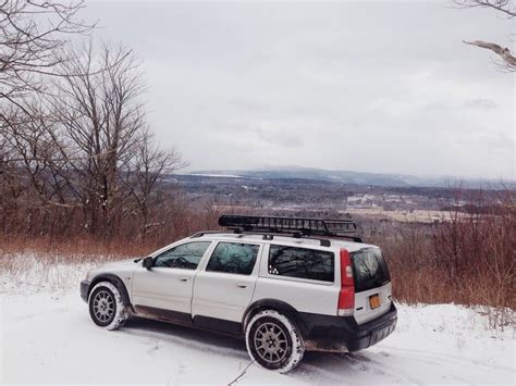 an suv parked on the side of a snow covered road with trees in the background