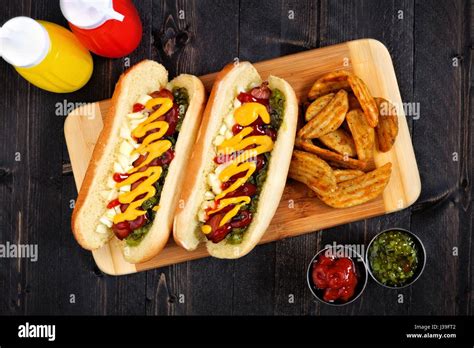 Two hot dogs fully loaded with toppings and potato wedges on wooden ...