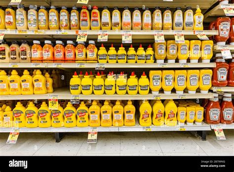 Assorted brands of yellow mustard sauce bottles fully stocked on shelves of the condiments aisle ...