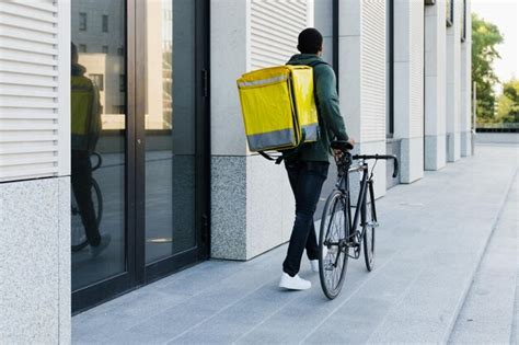 Premium Photo | The courier is walking with a big yellow backpack next to the bike outside