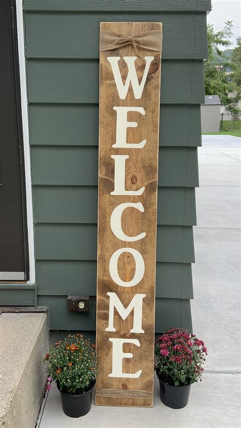 a wooden welcome sign sitting on the side of a house next to potted plants