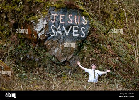 Mormon missionary posing under JESUS SAVES graffiti on exposed rock face next country road in ...